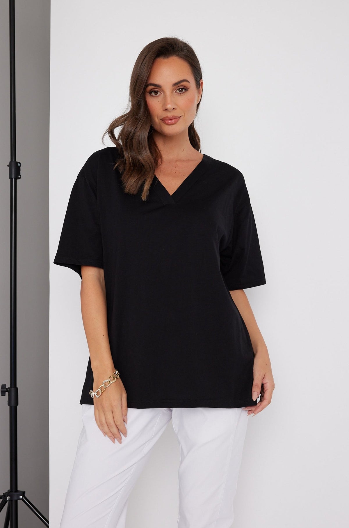 Woman modelling a loose black top with white trousers in a studio