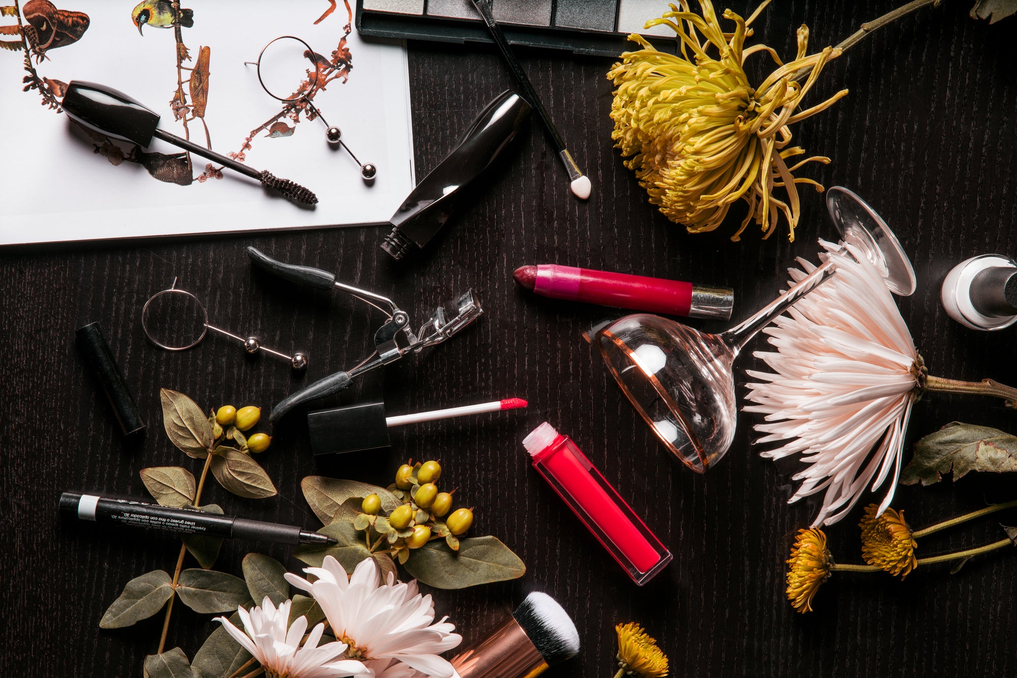 Cosmetics and makeup brushes arranged with flowers on a dark surface