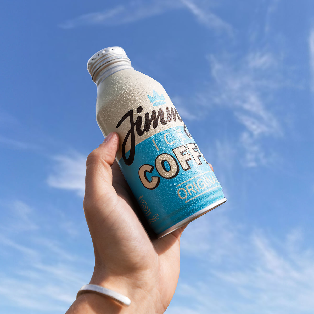 Hand holding a bottle of Jimmy's Original Iced Coffee against a blue sky