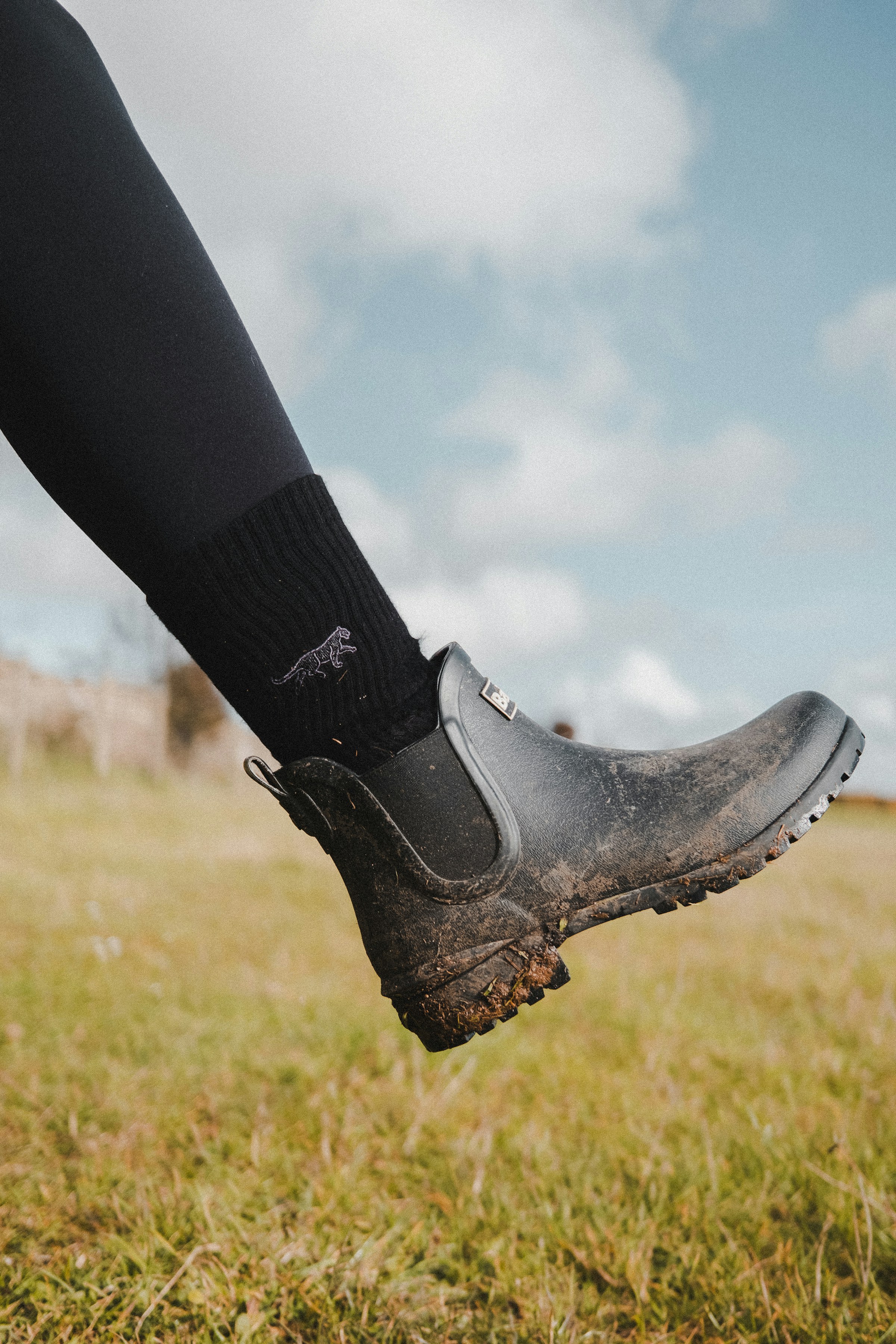 A person wearing rugged black lace-up boots while walking through a grassy field