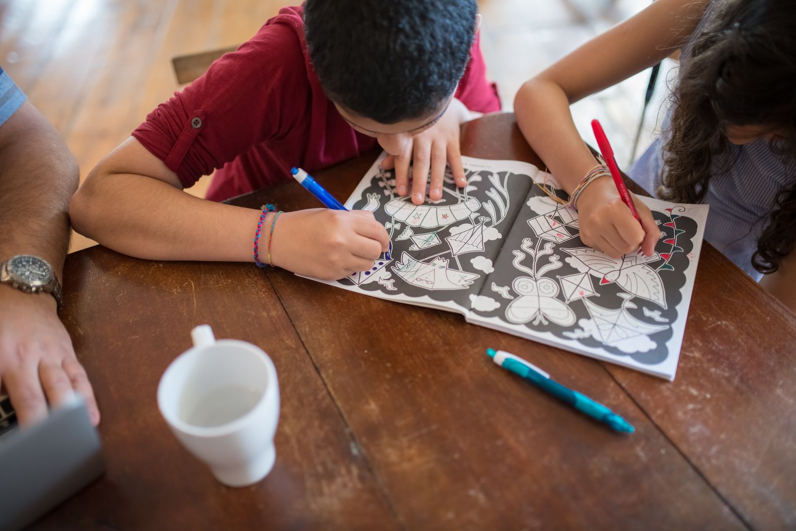 Two children colouring an illustrated activity book with coloured pens