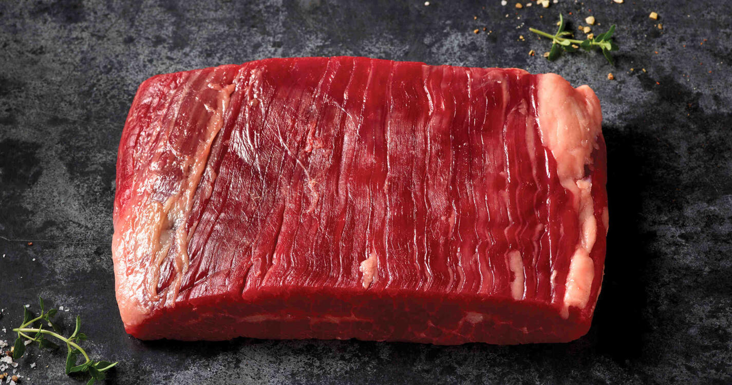 Raw domestic Wagyu flank steak on a dark stone surface