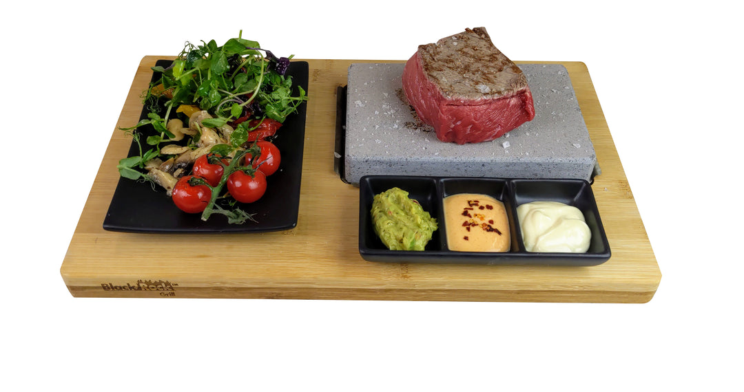 Steak cooking on a hot stone beside salad and small dishes of condiments