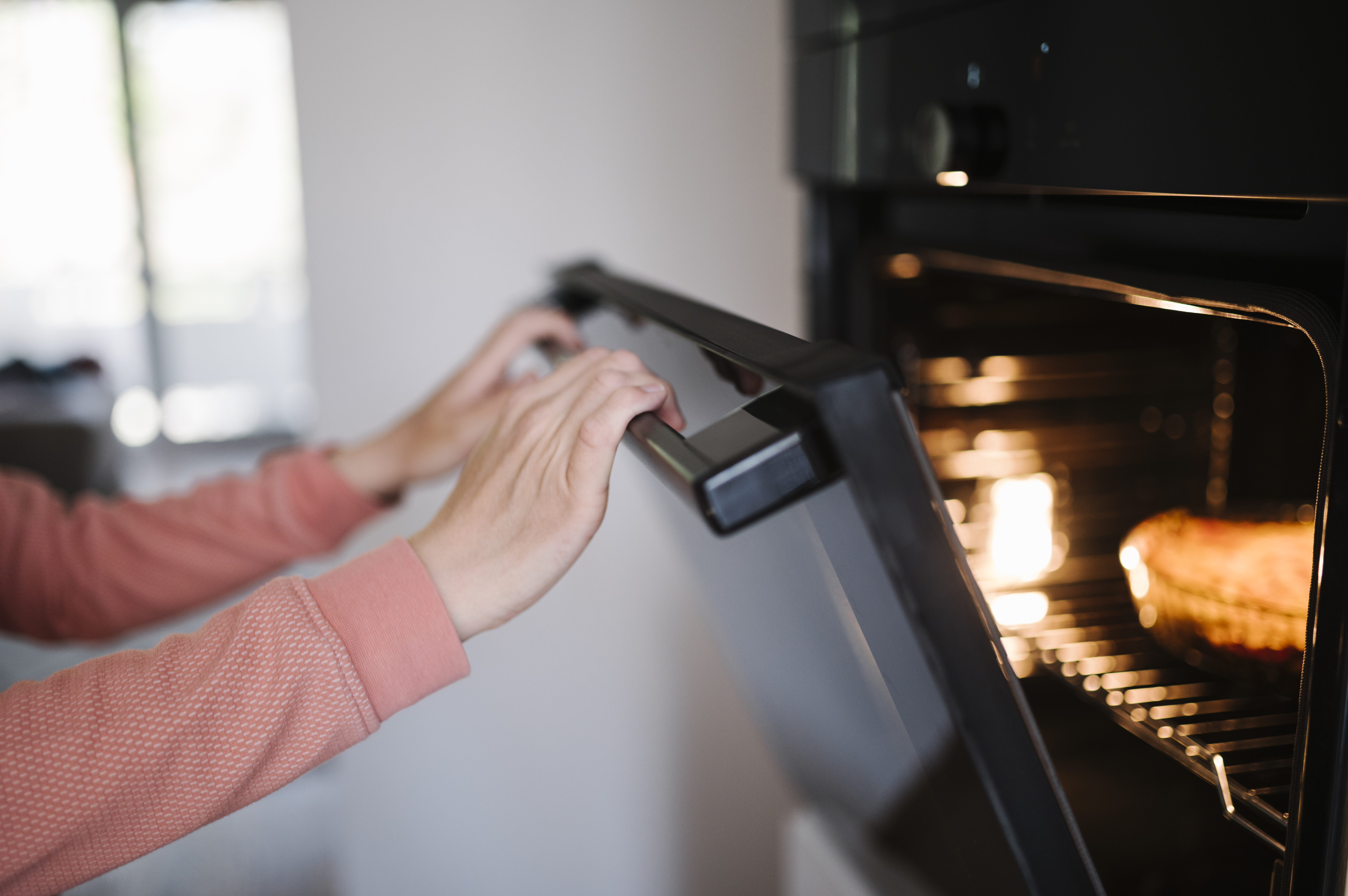 Person opening a modern built-in oven containing a roasting dish