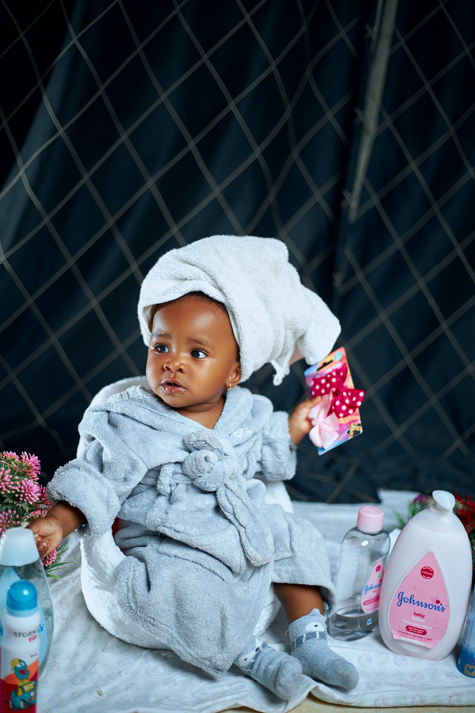 Baby in a bathrobe seated beside bottles of baby-care products