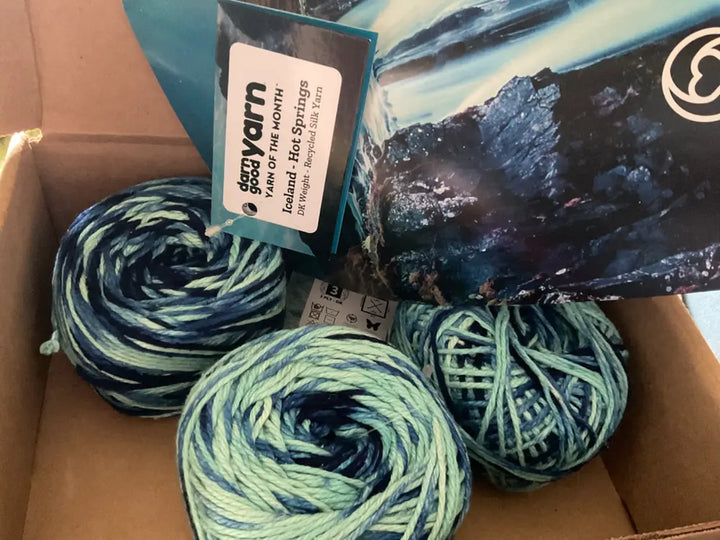 Blue and green yarn skeins arranged inside an open subscription box