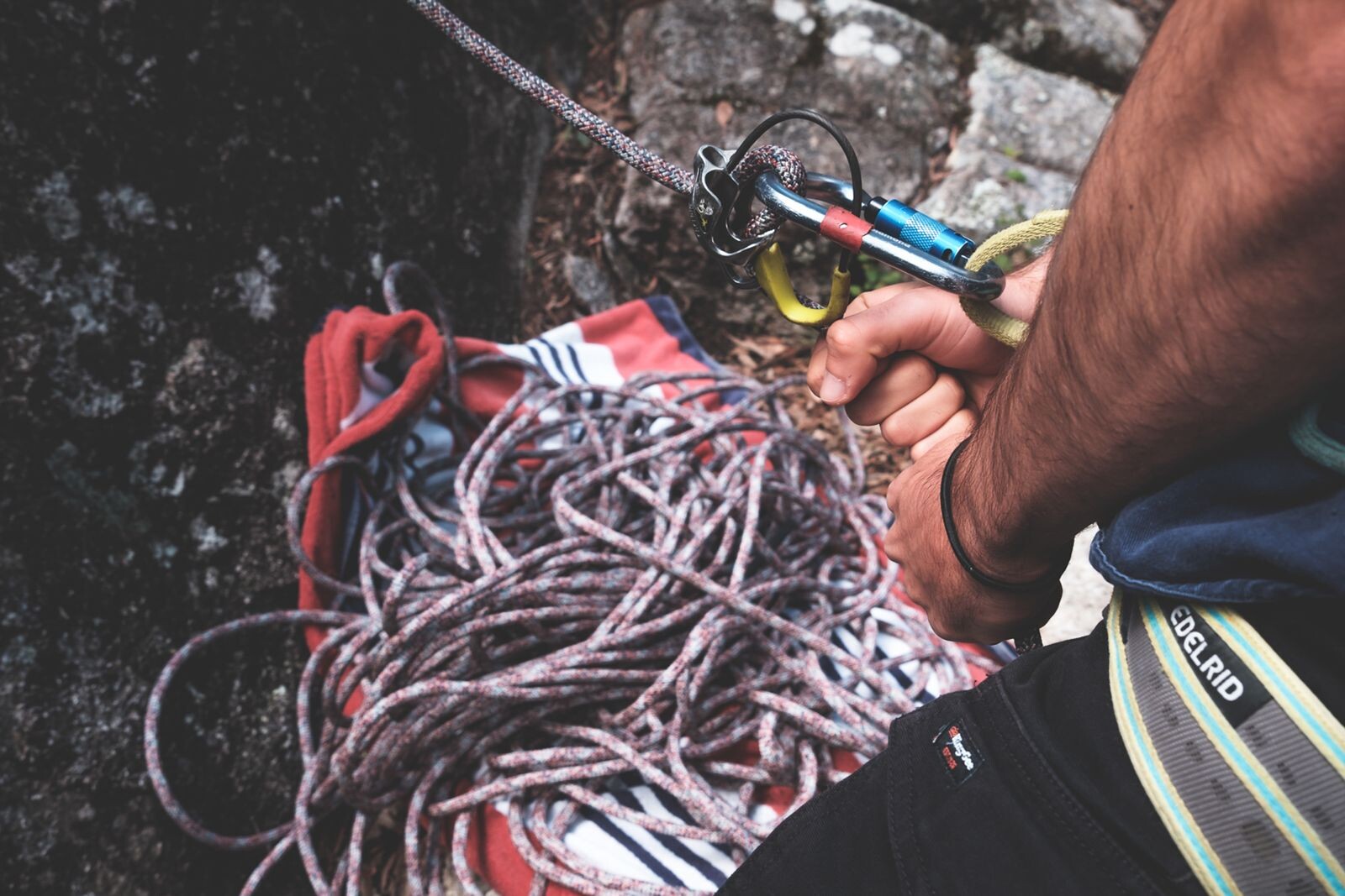 Climber handling a coiled rope and carabiners beside a rock face