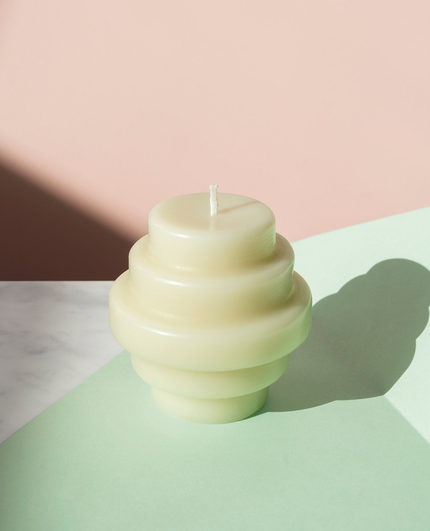 Pale green sculptural candle casting a shadow across a pastel tabletop