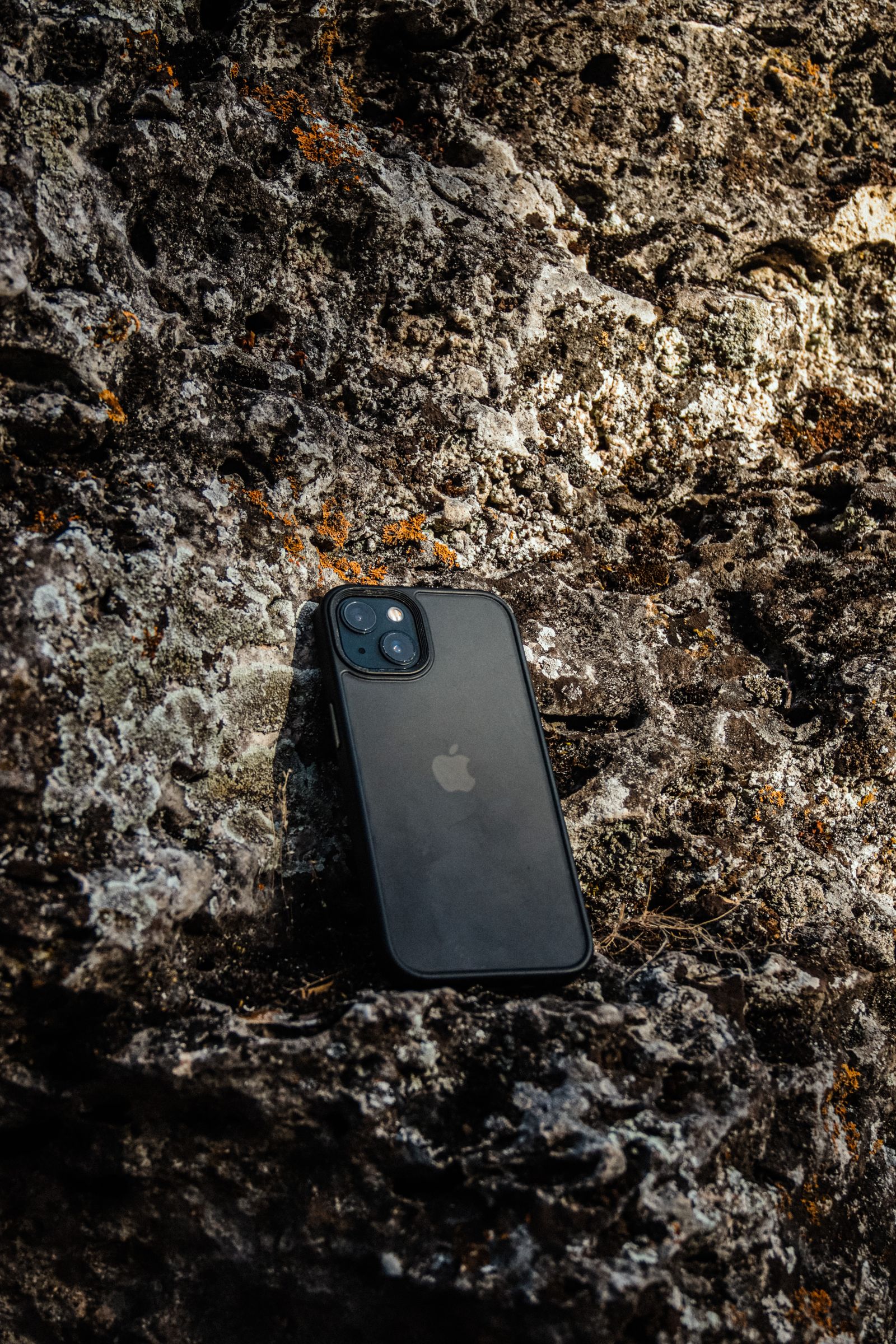 Black smartphone lying face down on textured rock outdoors