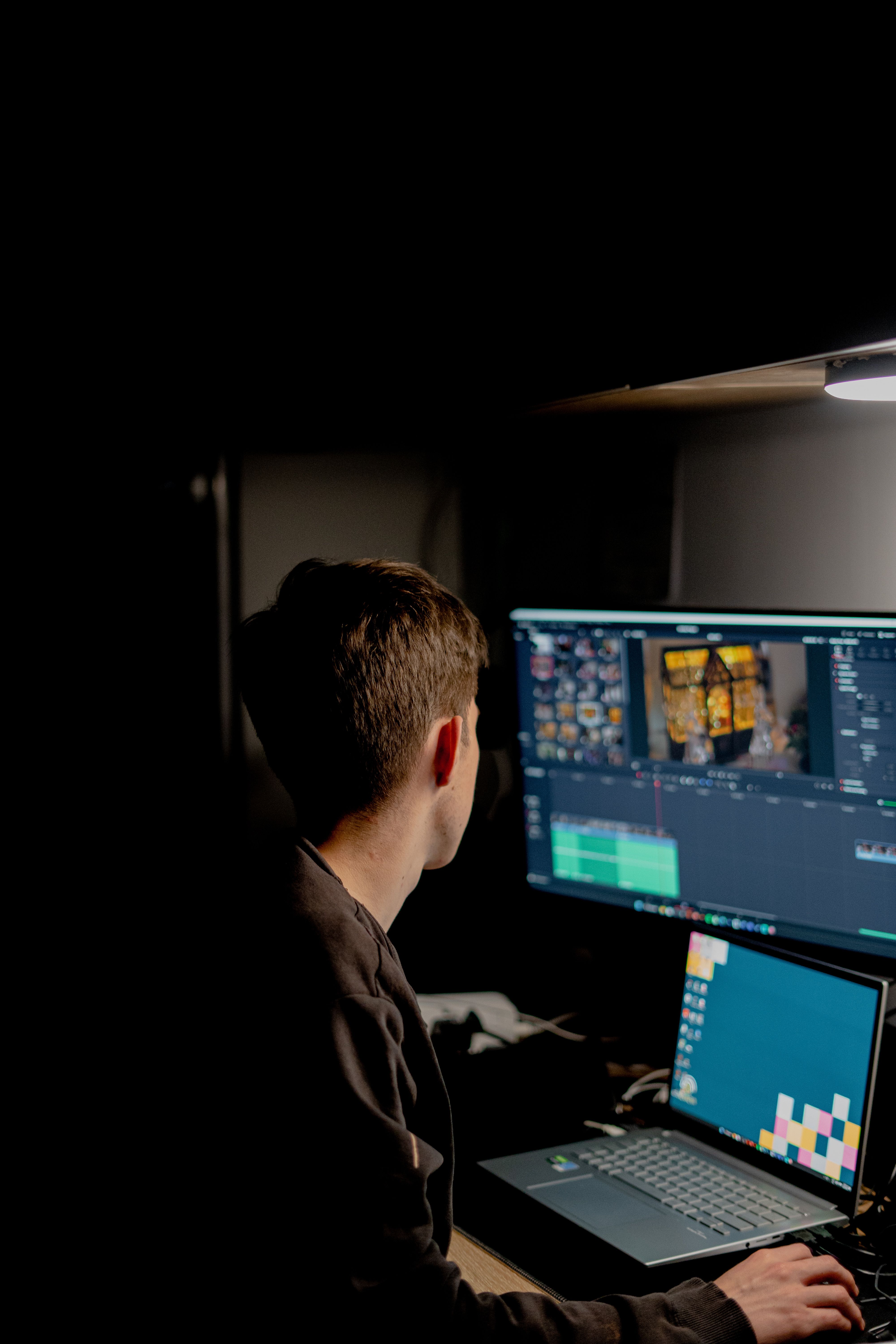 Person editing video at a desk with two computer monitors in a dark studio