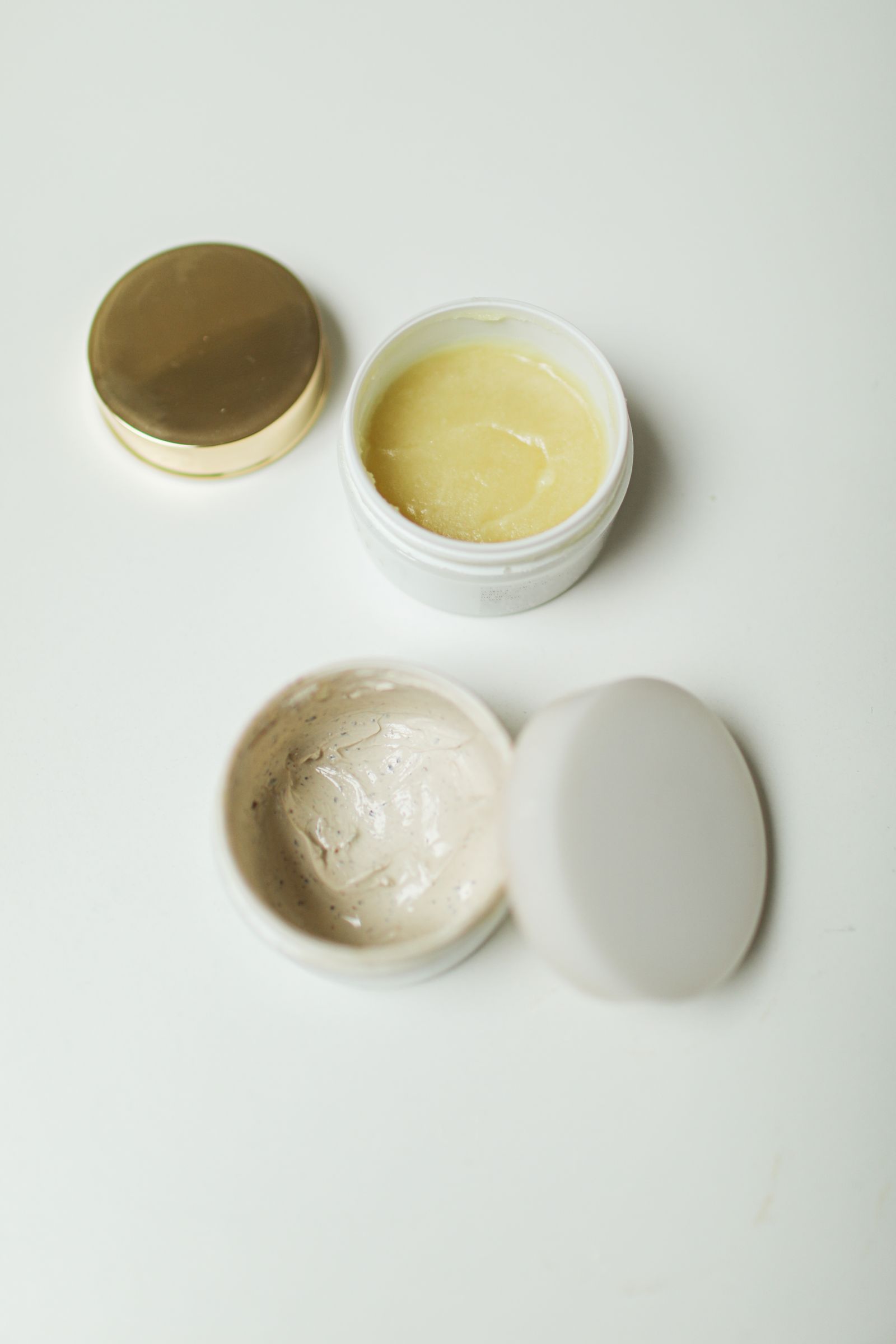 Open jars of white skincare cream arranged on a pale surface