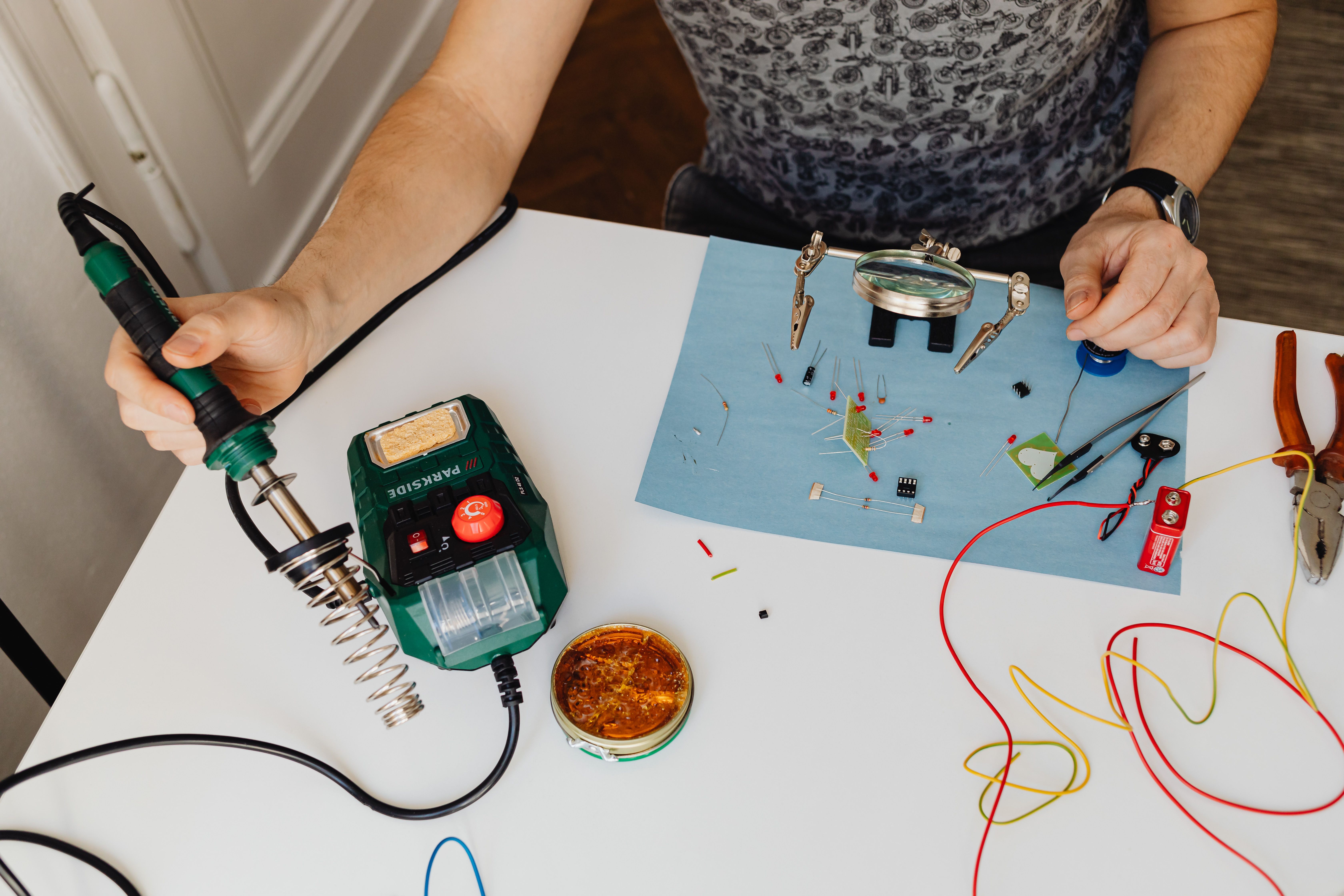 Electronics hobbyist soldering wires beside a multimeter and circuit board