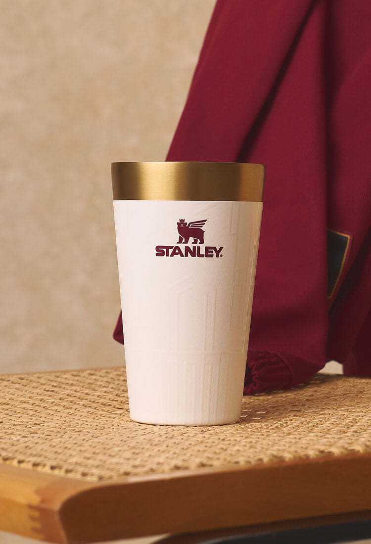Cream Stanley insulated cup on a woven table with red fabric behind it
