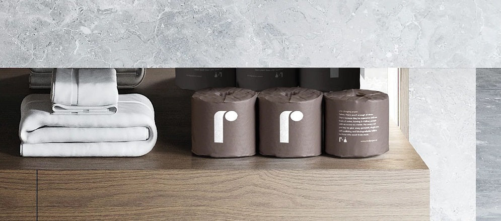 Bathroom shelf arranged with folded towels, paper rolls, and Reel paper products