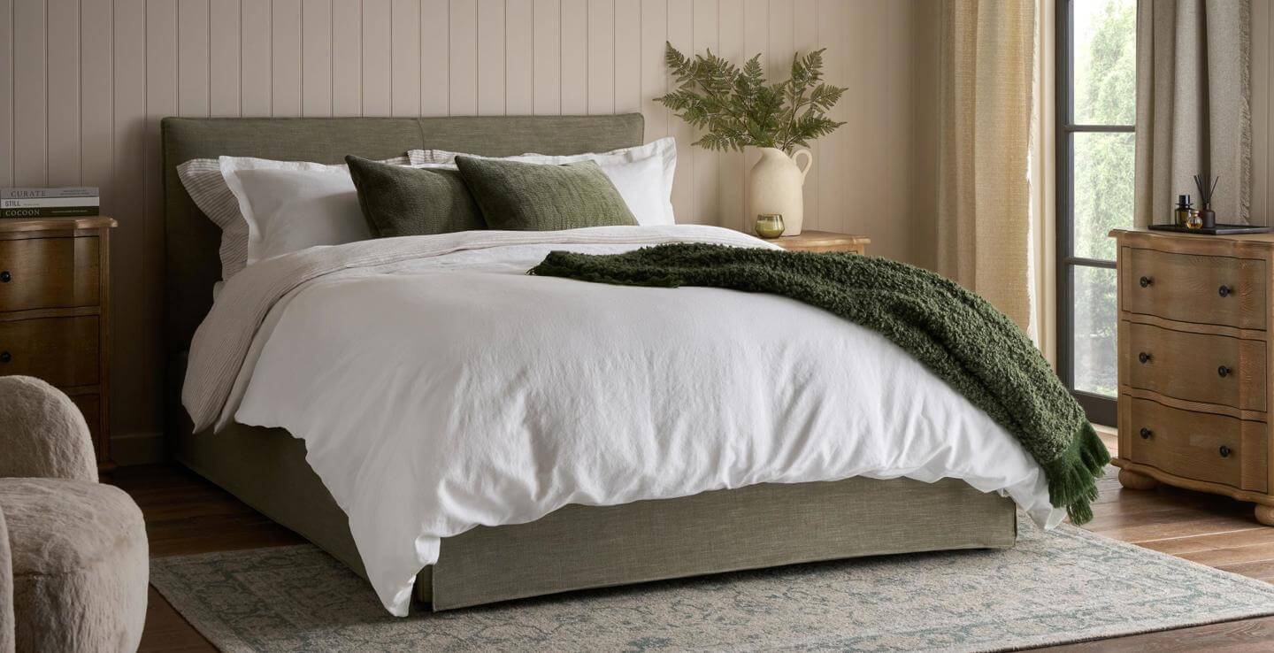 Upholstered bed dressed with white bedding and a dark green throw