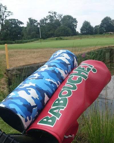 Blue camouflage and red golf club headcovers resting beside a golf course