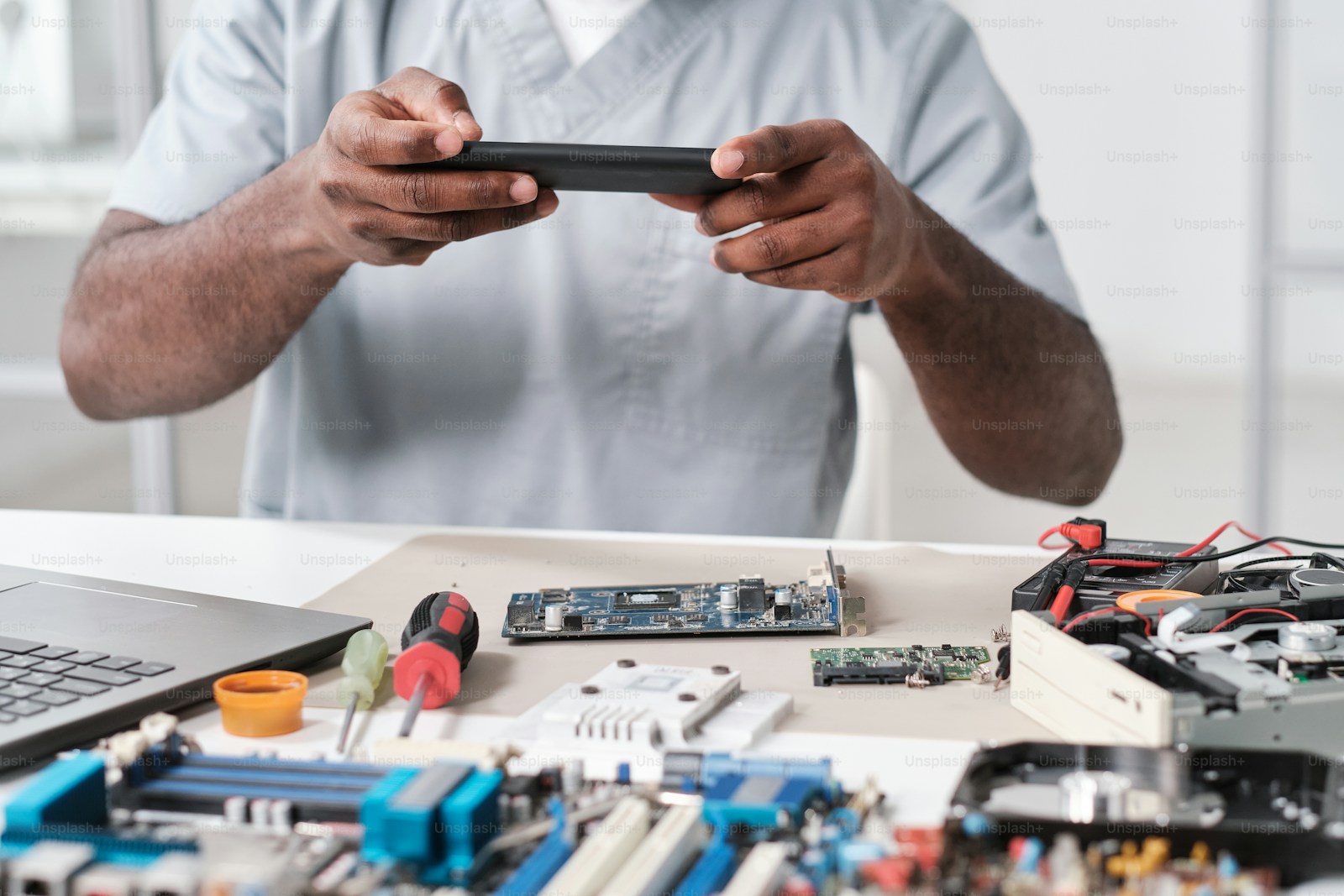 Technician holding a smartphone above an electronics repair workbench