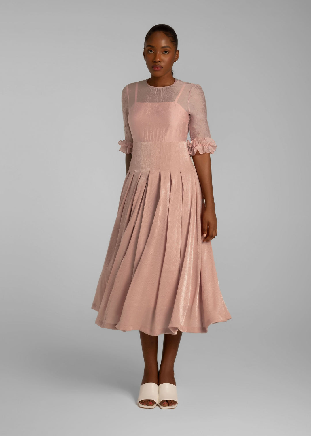 Model wearing a pale pink mid-length dress with pleats and sheer short sleeves
