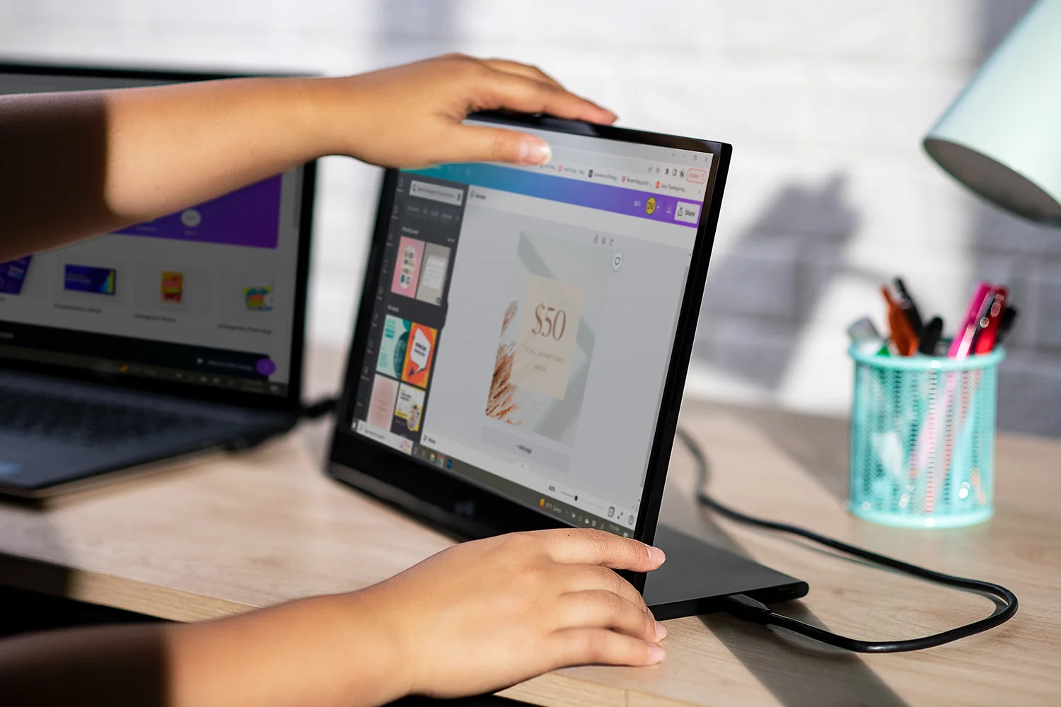 Person positioning a slim portable monitor beside a laptop on a desk