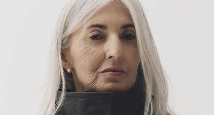 Close editorial portrait of a silver-haired woman wearing a high black fashion collar