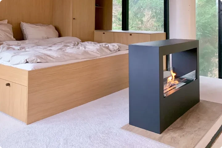 Freestanding black bioethanol fireplace burning beside a wooden bed