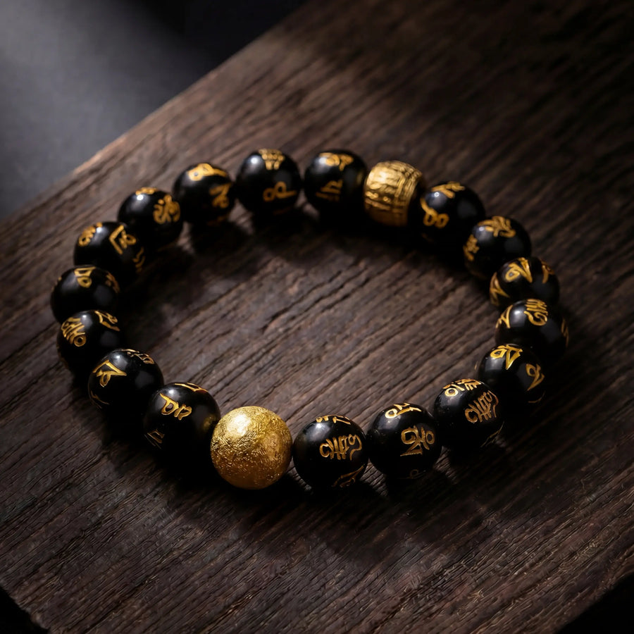 Black and gold mantra bead bracelet resting on a dark wooden surface.