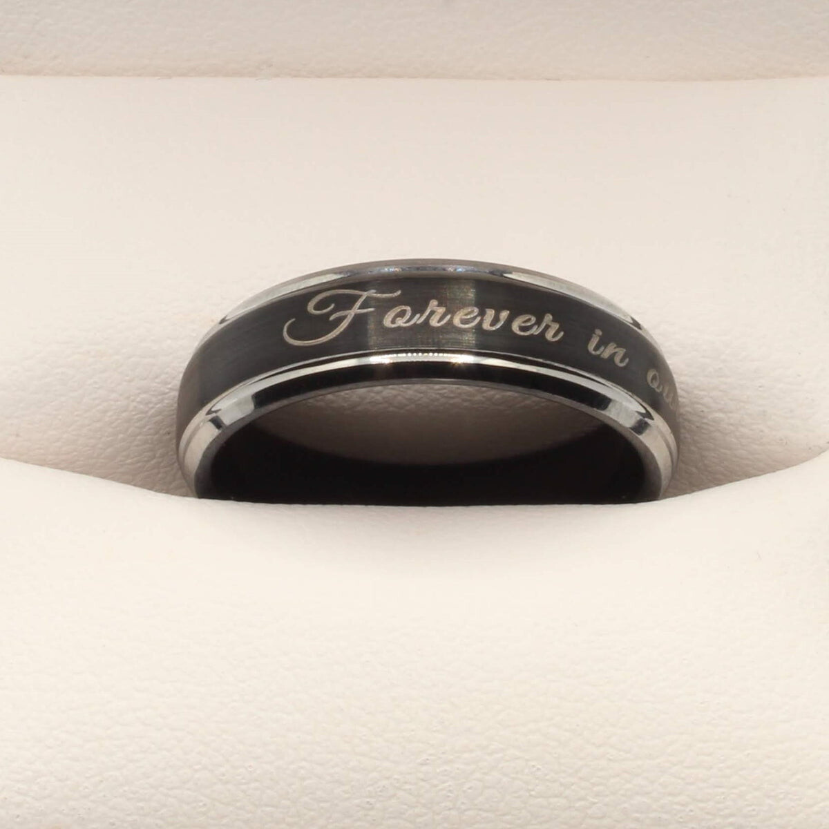 Dark memorial ring with a silver inscription resting in a ring box