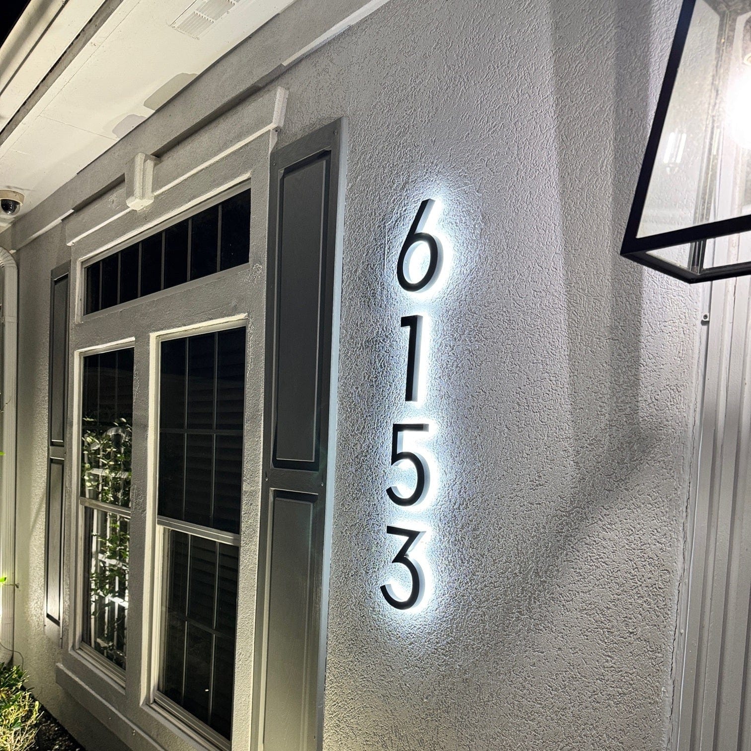 Backlit black house numbers glowing on a gray stucco exterior wall at night