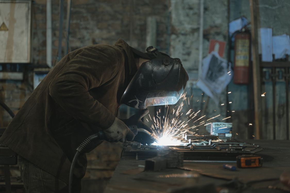Welder in protective gear working at a bench as bright sparks fly