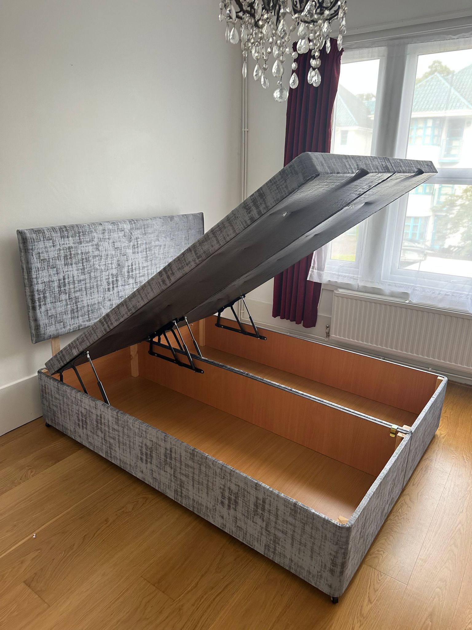 Grey upholstered end-lift ottoman bed open to show its under-bed storage compartment