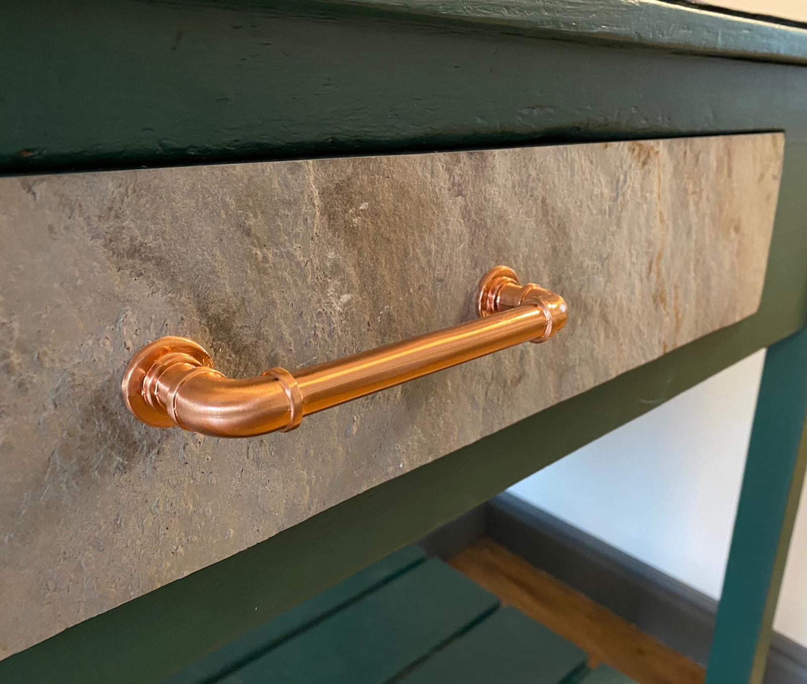 Close view of natural stone veneer fitted to a green cabinet drawer with a copper handle