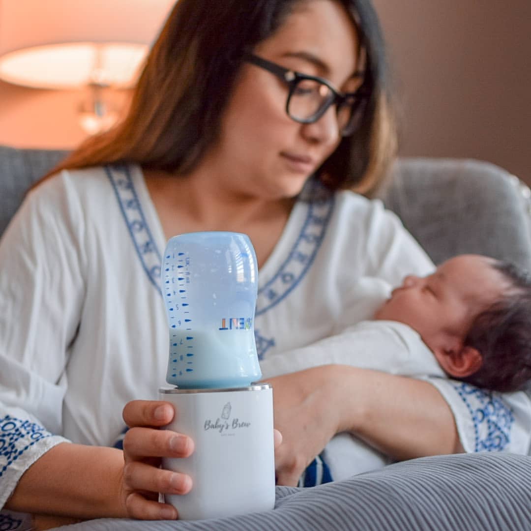 Mother holding her infant while using a Baby’s Brew portable bottle warmer