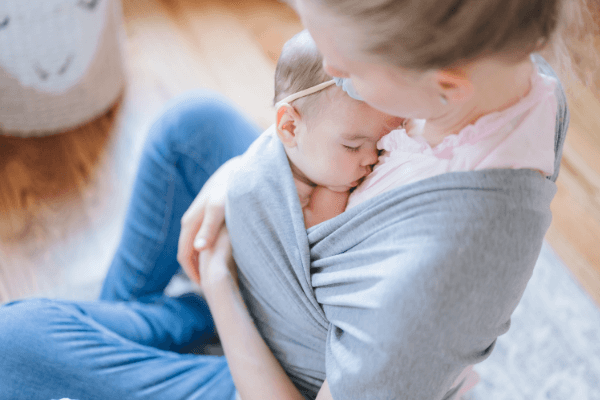 Mother carrying her sleeping infant in a gray baby wrap