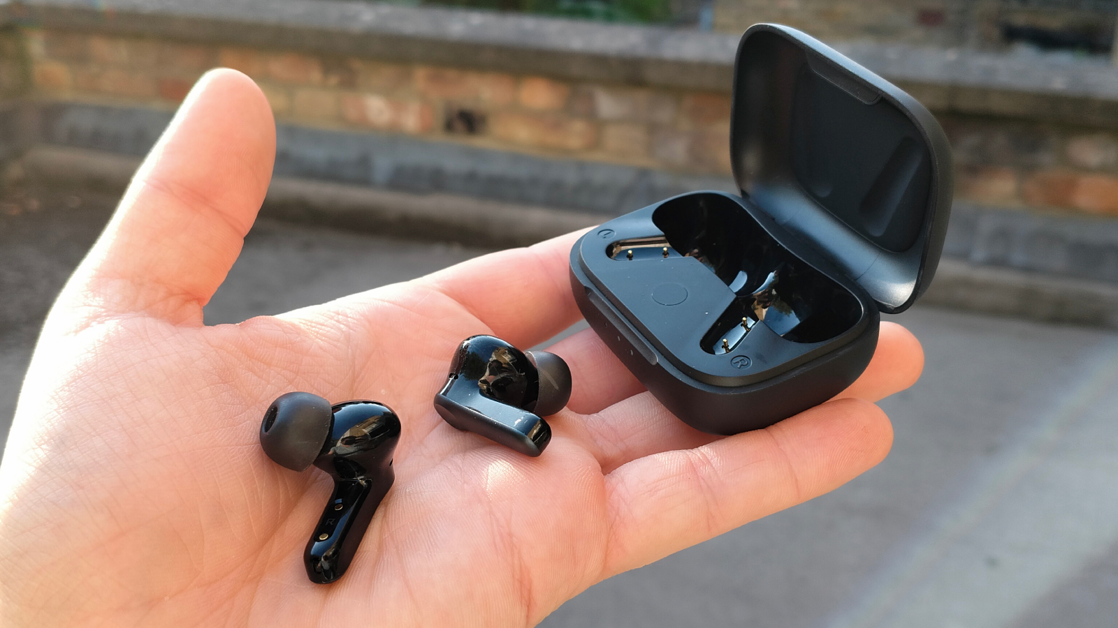 Black EarFun wireless earbuds and open charging case held in a person's hand