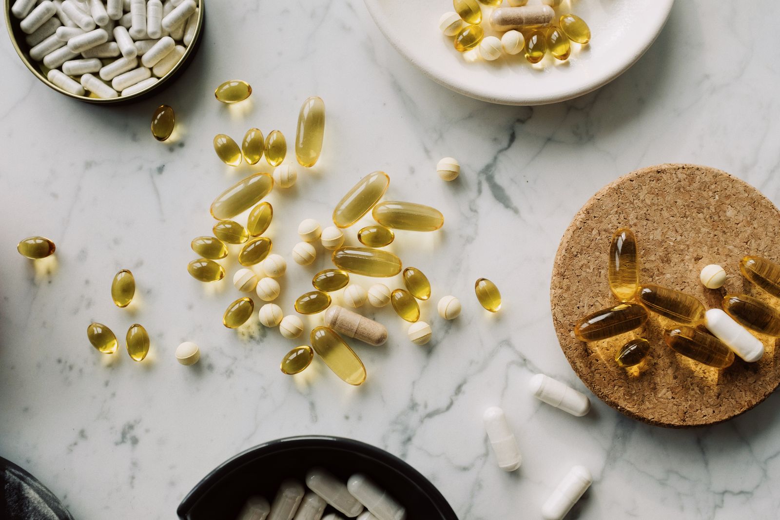 Assorted vitamin and supplement capsules arranged in open containers on marble