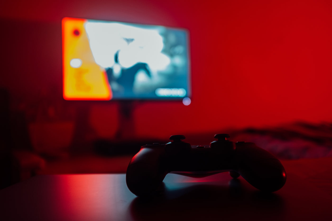 Game controller on a table facing a blurred television in a red-lit room